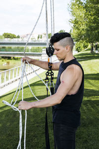 Side view of male gymnast in activewear preparing aerial straps for training in summer park