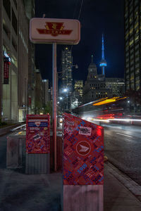 Illuminated road sign on city street by buildings at night