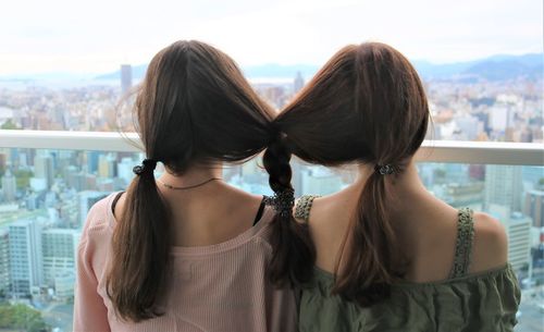 Rear view of sisters with braided hair against window