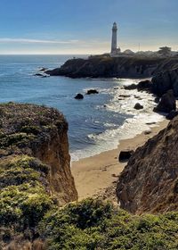 Pigeon point lighthouse in background with ocean and rocks in foreground sunny day, blue sky