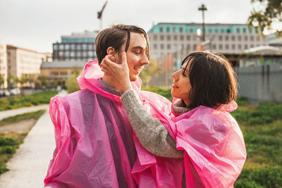 Happy young couple wearing pink raincoat in city