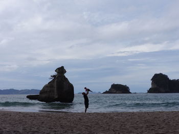 Side view of father playing with baby on shore against cloudy sky