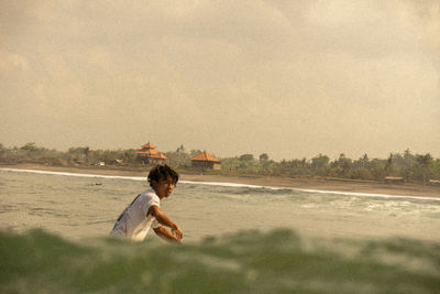 Side view of boy sitting on land against sky