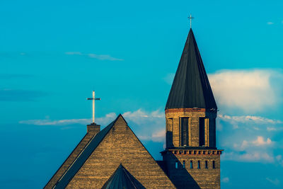 Low angle view of cross amidst buildings against sky