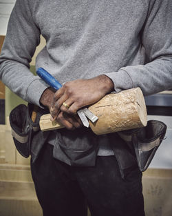 Midsection of carpenter holding wood and chisel