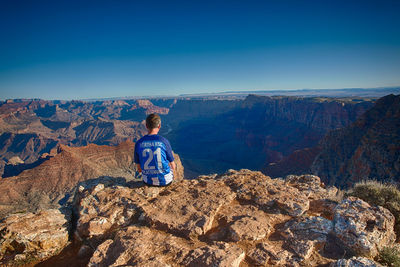 Rear view of man standing on mountain against clear blue sky