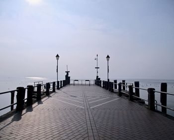 Street lights on footpath by sea against sky