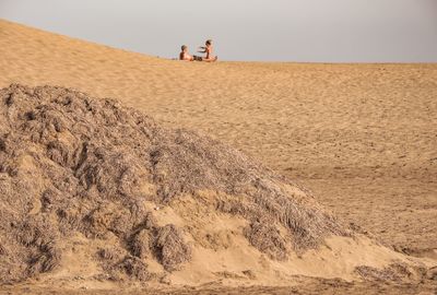 People sitting on sand dune in desert against sky