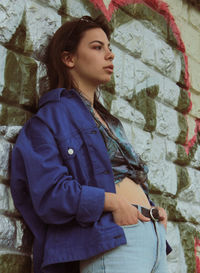 Young woman looking away while standing against wall