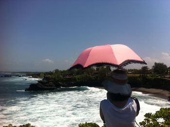 Rear view of man holding pink umbrella at beach