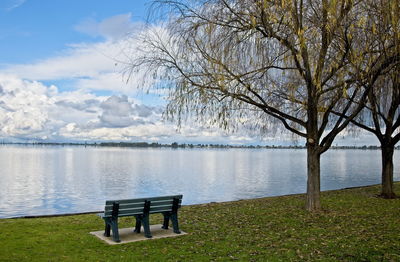 Empty bench by lake against sky