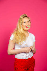 Portrait of young woman standing against pink background