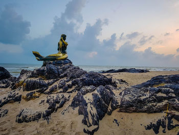 Mermaid statue on rock at beach against sky