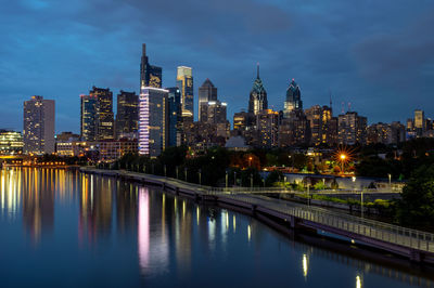 Illuminated buildings by river against sky in city at night