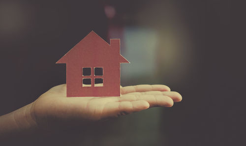 Close-up of hand holding small house against building