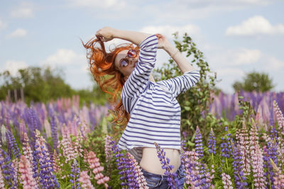 Young beautiful woman with redhead dancing in the field of flowers lupine