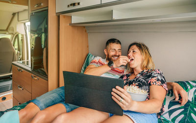 Man feeding his girlfriend a popcorn watching a movie on the tablet in their camper van