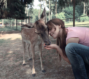 Woman feeding deer while crouching on field