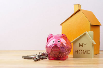Close-up of piggy bank with model homes on table against white background