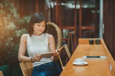 Young woman using mobile phone while sitting on table