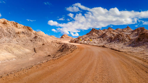 Dirt road at desert against sky
