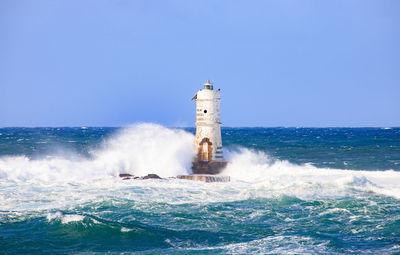 Lighthouse by sea against clear sky