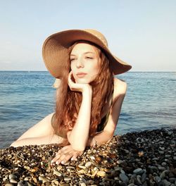 Beautiful young woman relaxing on shore at beach against sky