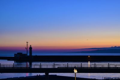 Silhouette lighthouse by sea against sky during sunset