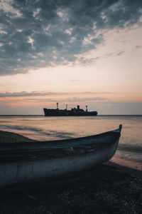 Boat moored at beach against cloudy sky during sunset