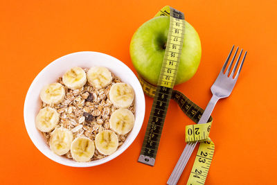Muesli with banana on orange background with apple and measuring tape