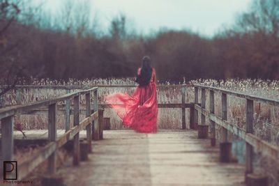 Woman walking on railing by bridge against sky