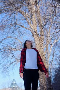 Low angle view of woman standing against bare tree