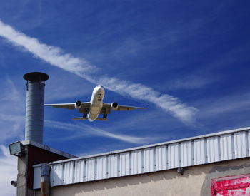 Low angle view of airplane flying by building against sky