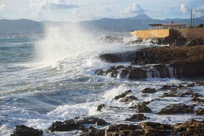 Waves splashing on rocks against sky