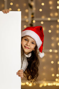 Portrait of smiling young woman in traditional clothing standing against illuminated christmas tree