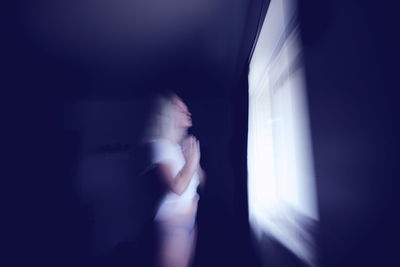 Blurred motion of woman standing against wall at night