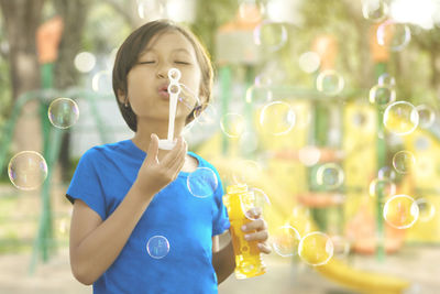 Girl blowing bubbles while standing in playground