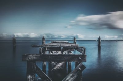 Old damaged pier in sea against sky