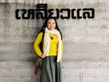 Portrait of a smiling young woman standing against wall