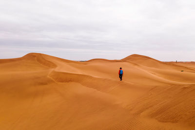 Rear view of man standing on sand at desert