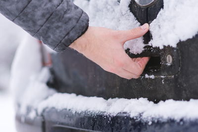 Cropped hand of man opening car trunk door during winter