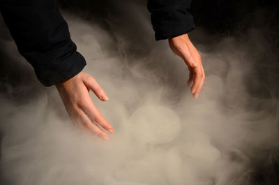 Cropped hands of woman amidst smoke over black background
