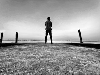 Rear view of silhouette man standing on sea shore against sky