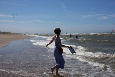 Full length side view of woman walking at beach against sky