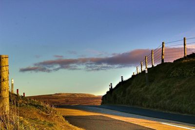 Road by fence against blue sky