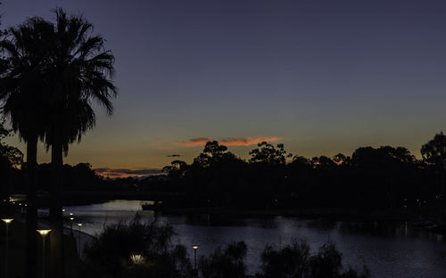 Silhouette palm trees by lake against sky during sunset