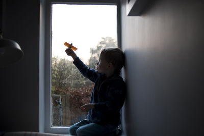 Boy playing with toy while kneeling by window at home