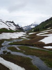 Scenic view of stream by snowcapped mountains against sky