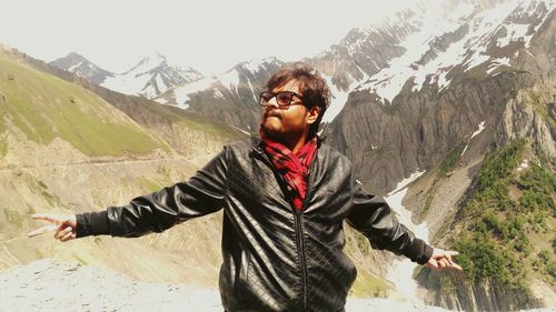 Man with arms outstretched standing against mountain during sunny day