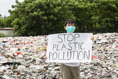 Portrait of boy holding poster against plastic garbage